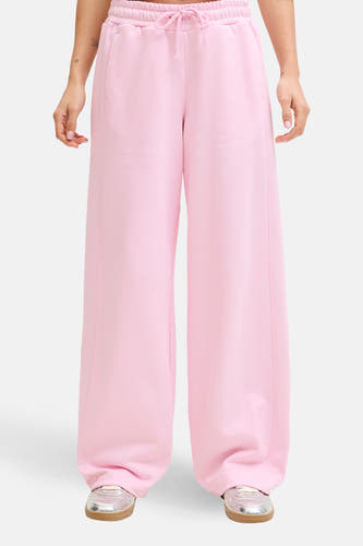 Pantalon de jogging rose de JJXX, à jambes larges et avec un cordon de serrage à la taille, porté avec un t-shirt blanc et des chaussures argentées.
