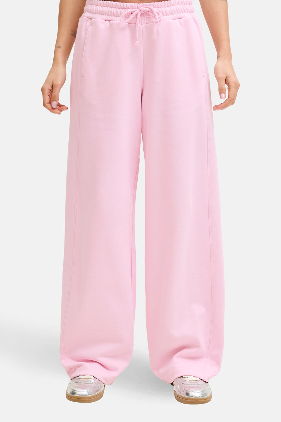 Pantalon de jogging rose de JJXX, à jambes larges et avec un cordon de serrage à la taille, porté avec un t-shirt blanc et des chaussures argentées.
