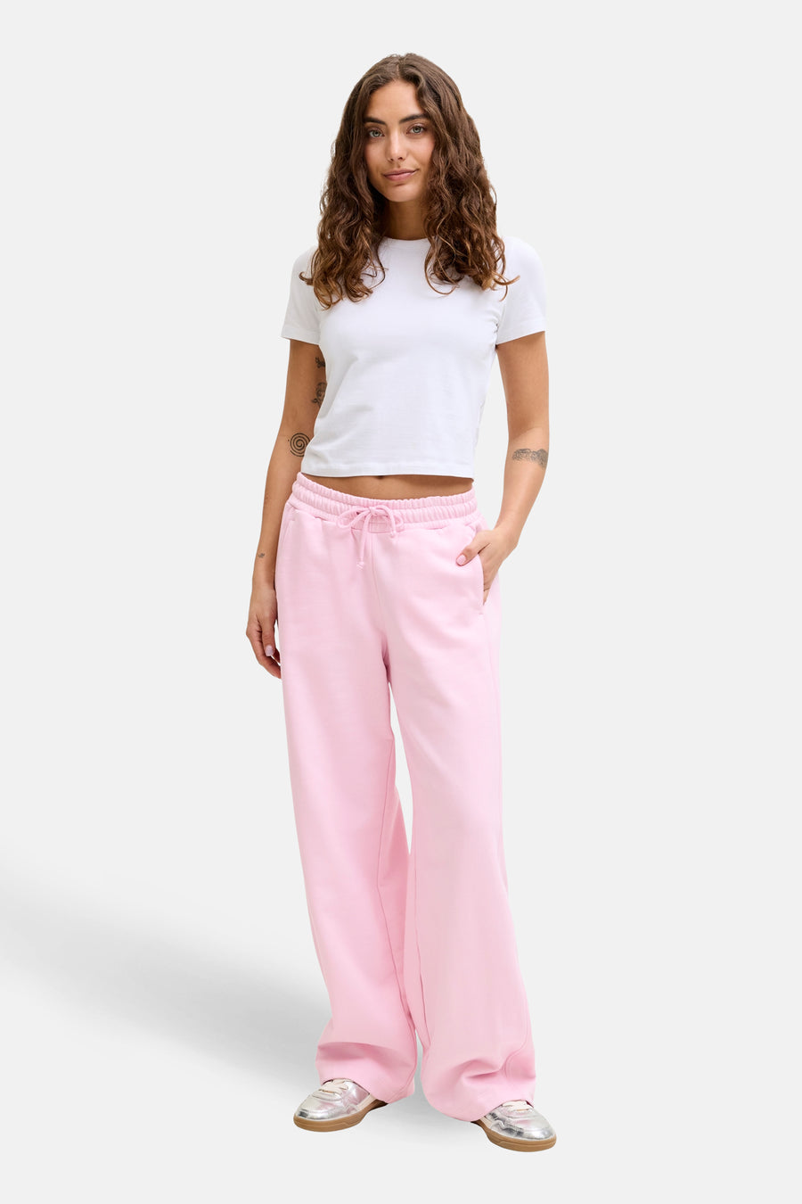 Roze joggingbroek van JJXX, met wijde pijpen en een trekkoord in de taille, gedragen met een wit T-shirt en zilveren schoenen.
