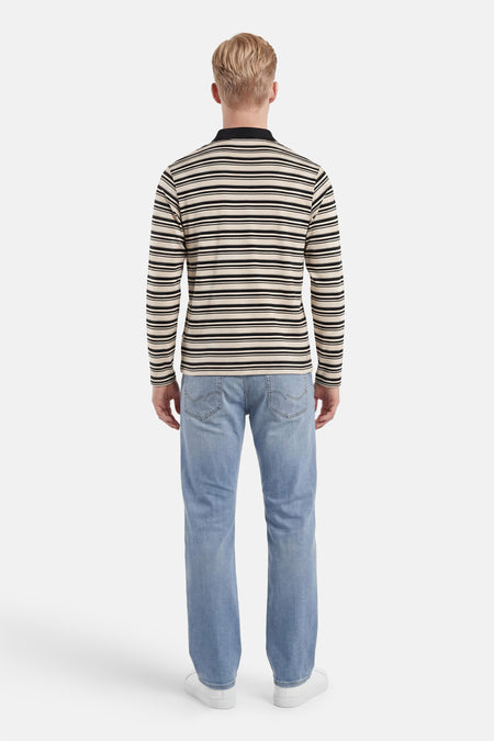 Polo multicolore à manches longues d'ORIGINALS BY JACK & JONES, avec des rayures horizontales crème et noires et un col polo noir, vue de dos sur un homme en jean et baskets blanches.
