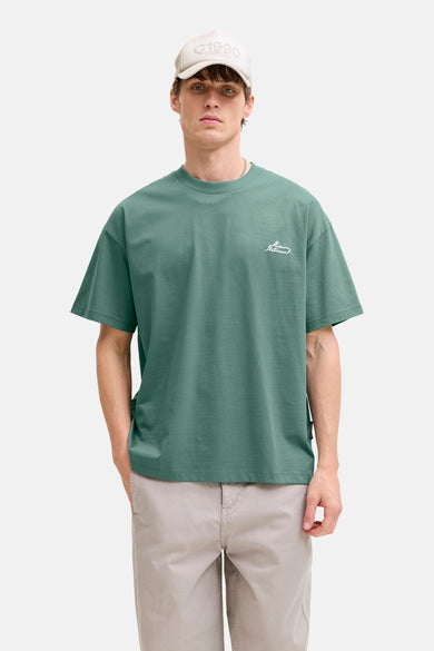 T-shirt vert à manches courtes CORE BY JACK & JONES, avec un petit imprimé, combiné avec un pantalon kaki et une casquette.