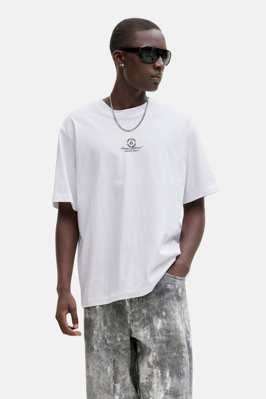 T-shirt blanc CORE BY JACK & JONES, avec un petit imprimé sur la poitrine, porté avec une chaîne argentée et un jean gris.