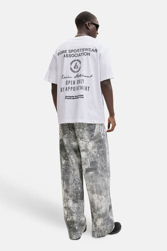 T-shirt blanc CORE BY JACK & JONES avec imprimé texte noir au dos, porté avec un jean gris.