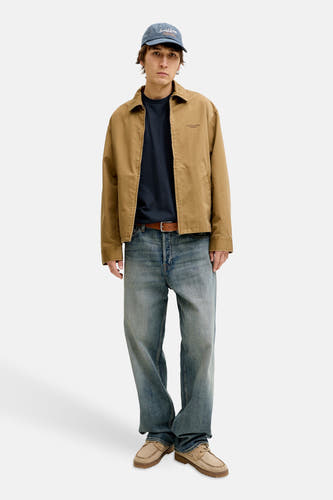 T-shirt bleu à manches courtes de PREMIUM BLUE by JACK & JONES, porté avec une veste marron, un jean et une casquette.