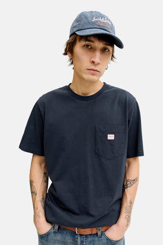 T-shirt bleu à manches courtes de PREMIUM BLUE by JACK & JONES, avec poche poitrine et porté avec un jean et une casquette.