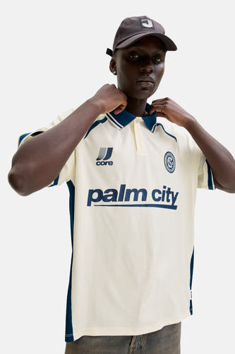 Polo blanche à manches courtes de CORE BY JACK & JONES, avec des accents bleus et un imprimé 'palm city'.