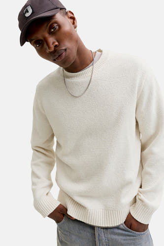Pull écru à col rond d'ORIGINALS BY JACK & JONES, avec une chaîne et une casquette foncée.