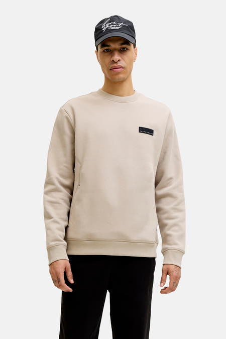 Pull beige de CORE BY JACK & JONES, à manches longues et col rond, combiné avec une veste noire et un jogging.
