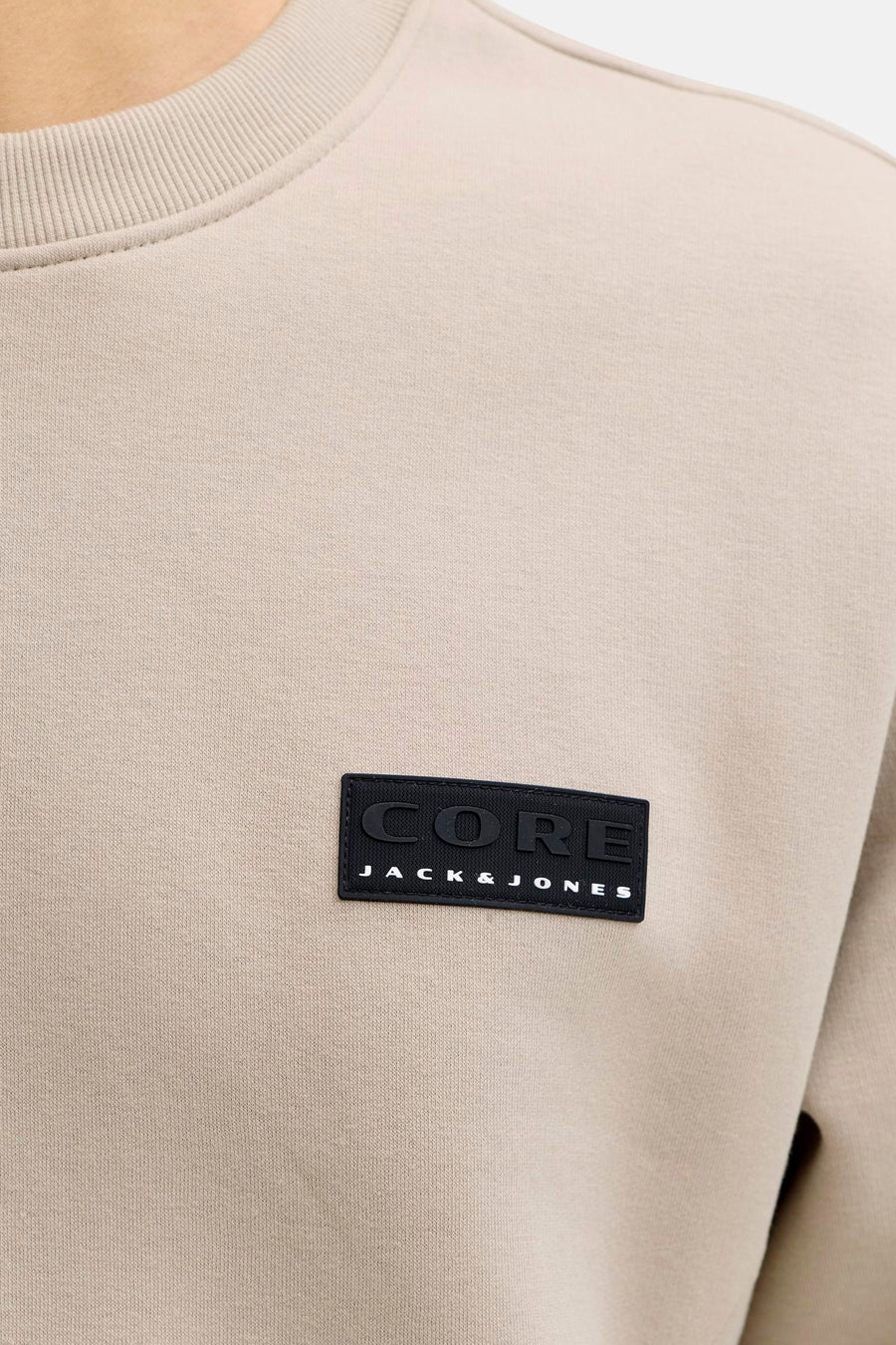 Pull beige de CORE BY JACK & JONES, avec étiquette de marque noire sur la poitrine et col rond.