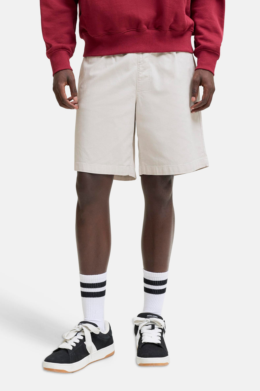 Short beige de JACK & JONES JEANS INTELLIGENCE, porté avec un sweat-shirt rouge, des chaussettes rayées et des baskets noires.