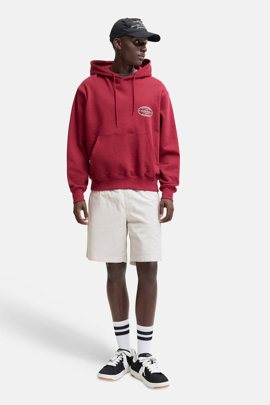 Short beige de JACK & JONES JEANS INTELLIGENCE, porté par un mannequin avec un sweat à capuche rouge et des baskets.