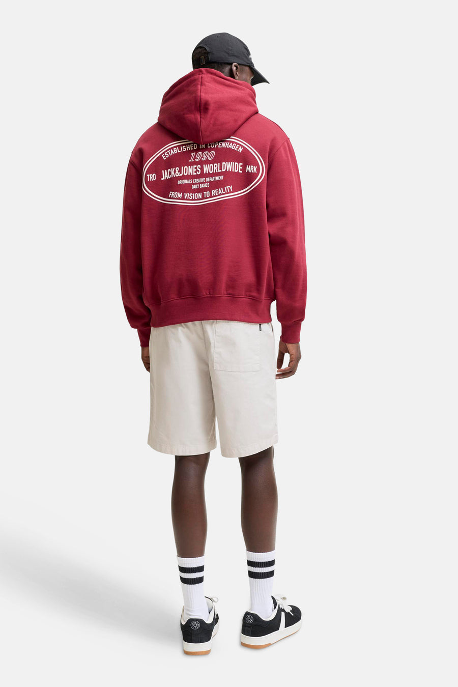 Short beige de JACK & JONES JEANS INTELLIGENCE avec une poche arrière, porté par un homme avec un sweat à capuche et des baskets, vu de dos.