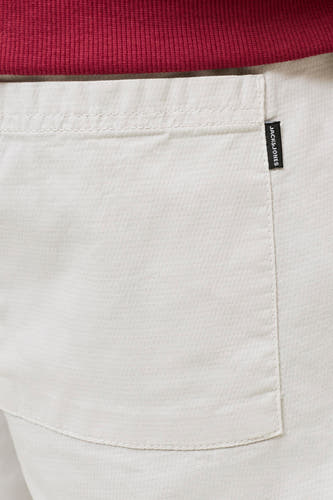 Short beige de JACK & JONES JEANS INTELLIGENCE avec une texture tissée, une poche visible avec étiquette noire et un tissu côtelé rouge au-dessus.