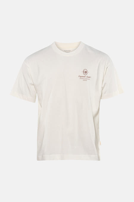 T-shirt blanc à manches courtes de Originals by Jack & Jones, avec petit logo sur la poitrine, combiné avec un jean bleu et des baskets grises.