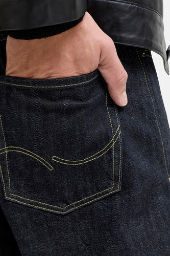 Jean en denim bleu foncé coupe droite de JACK & JONES JEANS INTELLIGENCE, avec une main dans la poche arrière et une veste en cuir.