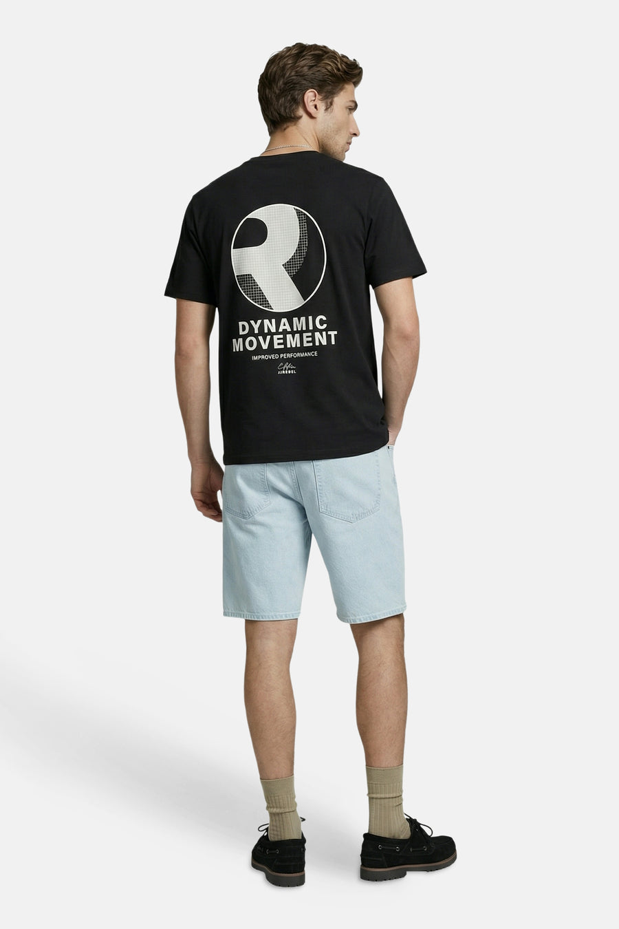 T-shirt noir JJREBEL avec grand imprimé graphique blanc d'un logo 'R' et le texte 'DYNAMIC MOVEMENT' dans le dos, porté par un homme en short en jean.