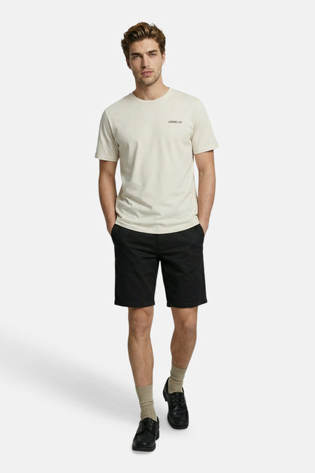 T-shirt beige JJREBEL à manches courtes avec imprimé 'JJREBEL/23', porté avec un short noir, des chaussettes beiges et des chaussures noires.