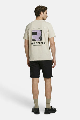 T-shirt beige de JJREBEL avec un logo graphique 'R' violet et noir dans le dos, porté par un homme avec un short noir.