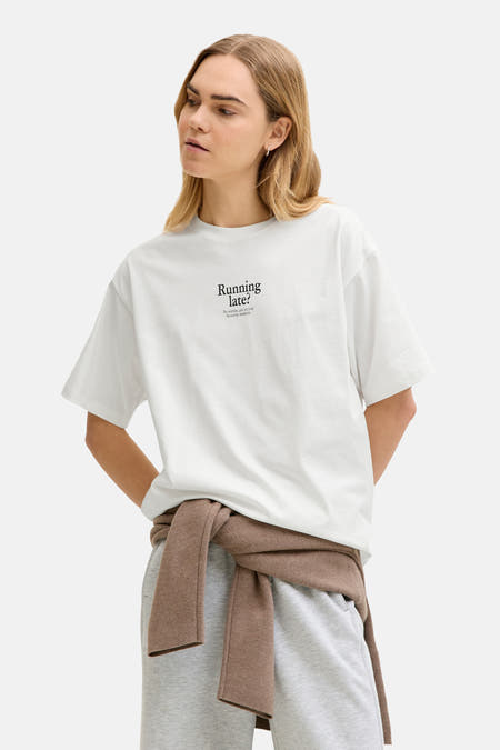 T-shirt blanc à manches courtes de JJXX, avec un imprimé, combiné avec un jogging gris et un pull marron.