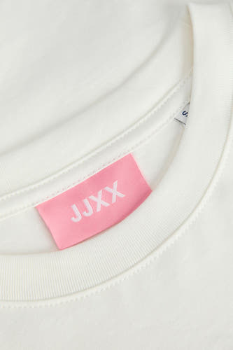 T-shirt blanc à manches courtes de JJXX, avec une étiquette rose dans le col et un design simple.