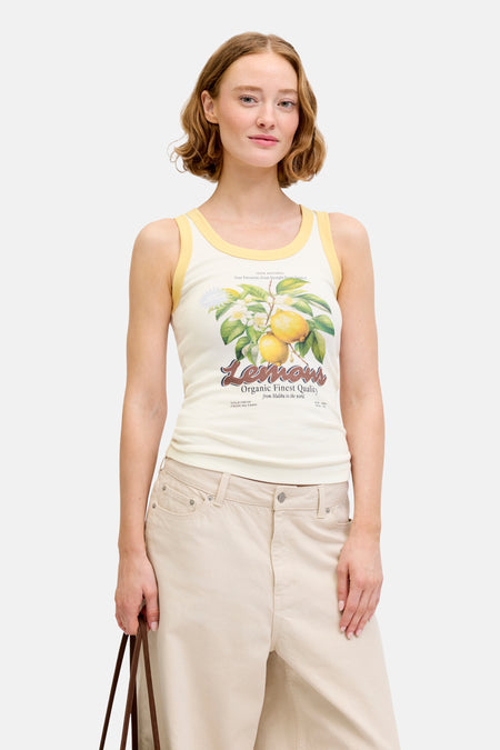 Débardeur écru de JJXX avec imprimé citron et passepoil jaune, porté avec un bermuda beige et un tote bag marron.