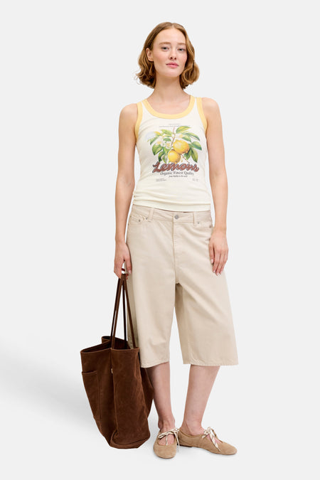 Ecru singlet van JJXX met citroenprint en gele biezen, gedragen met een beige bermuda en bruine totebag.