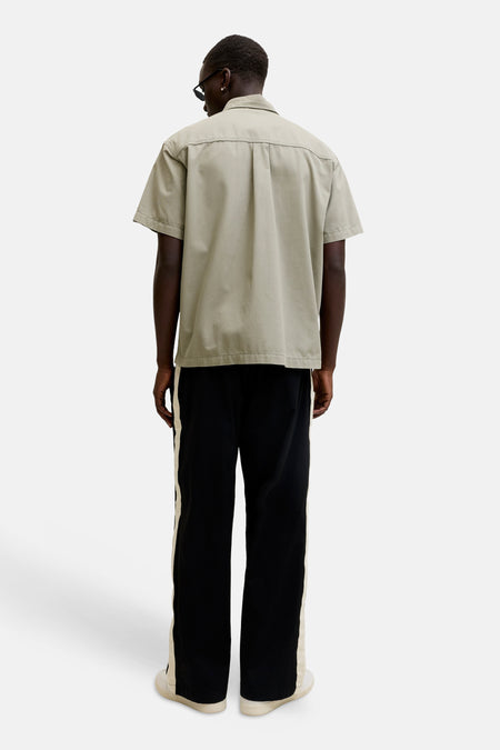 Chemise beige à manches courtes de CORE BY JACK & JONES, dos, avec plis dans le dos, portée avec un pantalon noir à bande latérale et des baskets blanches.
