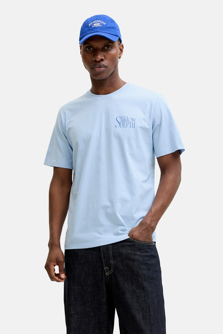 T-shirt bleu de ORIGINALS BY JACK & JONES, à manches courtes et avec un imprimé texte, combiné avec une casquette bleue et un jean foncé.