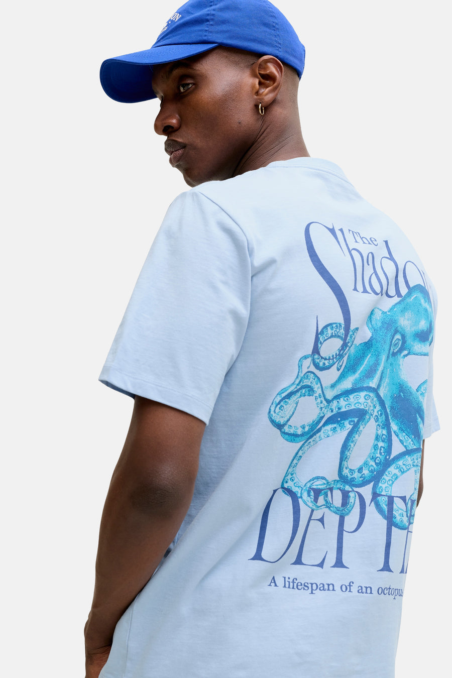 T-shirt bleu de ORIGINALS BY JACK & JONES, avec imprimé pieuvre et texte au dos, porté avec une casquette bleue.