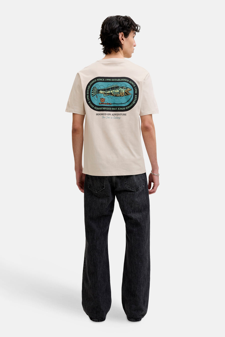 T-shirt beige de ORIGINALS BY JACK & JONES, avec un imprimé graphique au dos et porté avec un jean noir.