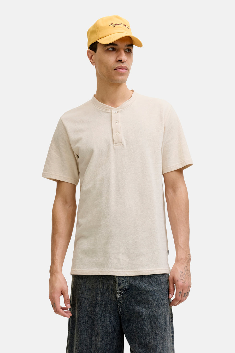 Beige korte mouwen T-shirt met knoopsluiting van PREMIUM by JACK & JONES, gedragen met gele pet en donkere jeans, front view