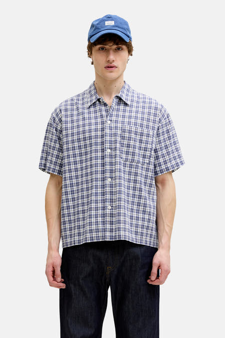 Chemise à carreaux bleus à manches courtes de ORIGINALS BY JACK & JONES, associée à un jean foncé et une casquette bleue.