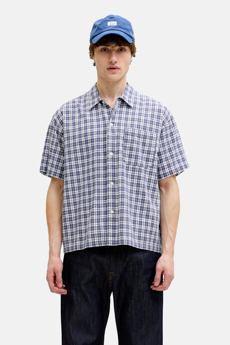 Chemise à carreaux bleus à manches courtes de ORIGINALS BY JACK & JONES, associée à un jean foncé et une casquette bleue.