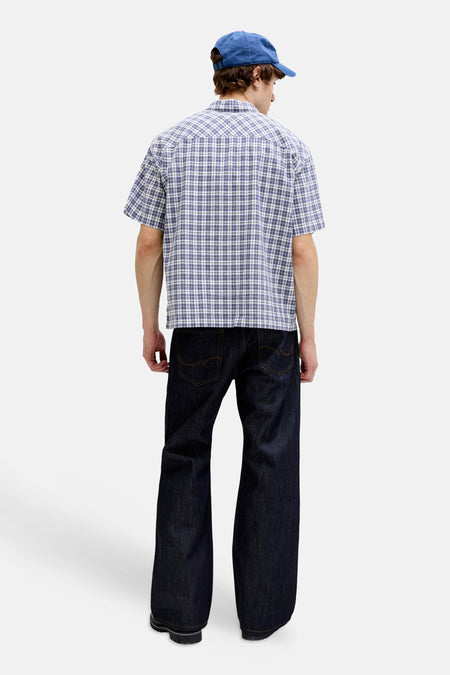 Chemise à carreaux bleus à manches courtes de ORIGINALS BY JACK & JONES, portée de dos avec un jean foncé et une casquette bleue.