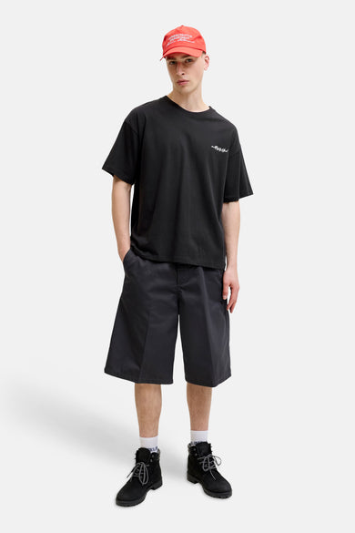 T-shirt noir à manches courtes de CORE BY JACK & JONES, avec imprimé blanc 'mid99 Club' sur la poitrine, combiné avec un short foncé et une casquette rouge.