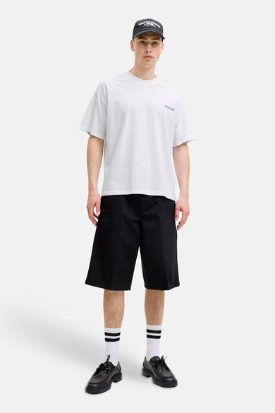 Wit T-shirt met korte mouwen van CORE BY JACK & JONES, met 'CORE 1980' print op de borst. Model draagt ook een zwarte pet, zwarte shorts en gestreepte sokken.
