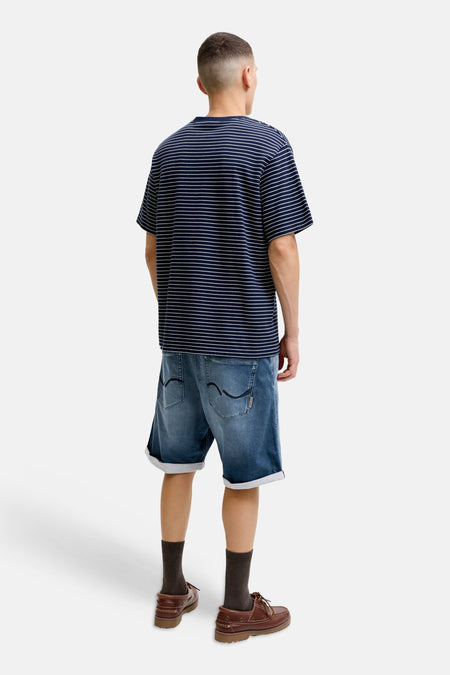 Midblauwe denim 5-pocket short van JACK & JONES JEANS INTELLIGENCE, achterzijde met opgerolde pijpen en zakken, gedragen met gestreept shirt en bruine schoenen