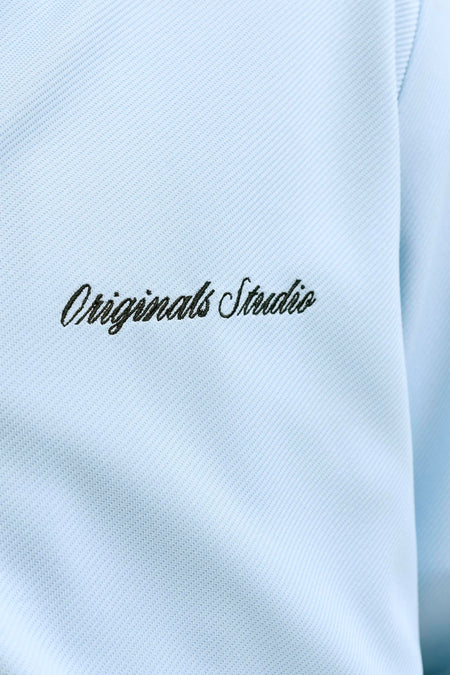 Gilet bleu de ORIGINALS BY JACK & JONES, gros plan avec texture côtelée, motif en diagonale et texte noir brodé 'Originals Studio'.