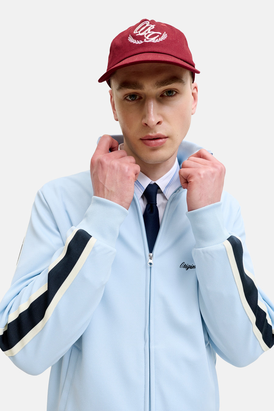 Gilet bleu clair de ORIGINALS BY JACK & JONES avec des rayures bleu foncé et crème sur les manches, fermeture éclair argentée et broderie "Origin" sur la poitrine.