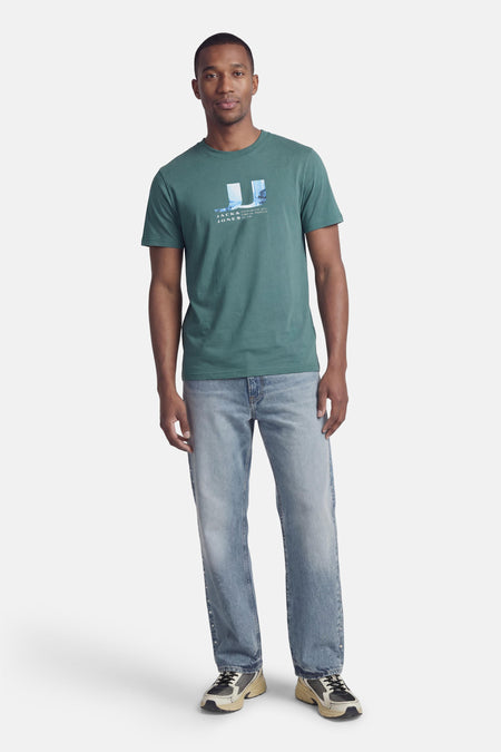 T-shirt vert à manches courtes CORE by JACK & JONES, avec un imprimé graphique sur la poitrine, porté avec un jean et des baskets.