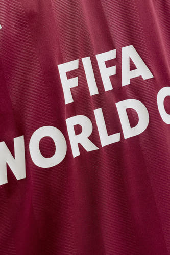 Gros plan d'un polo bordeaux de ORIGINALS BY JACK & JONES avec le texte blanc 'FIFA WORLD C' et de subtiles rayures tissées.