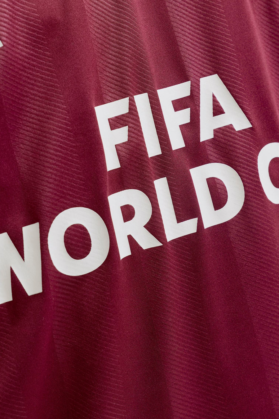 Gros plan d'un polo bordeaux de ORIGINALS BY JACK & JONES avec le texte blanc 'FIFA WORLD C' et de subtiles rayures tissées.