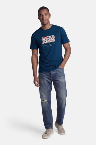 T-shirt bleu à manches courtes de CORE BY JACK & JONES, avec un imprimé graphique, combiné avec un jean troué et des baskets grises.