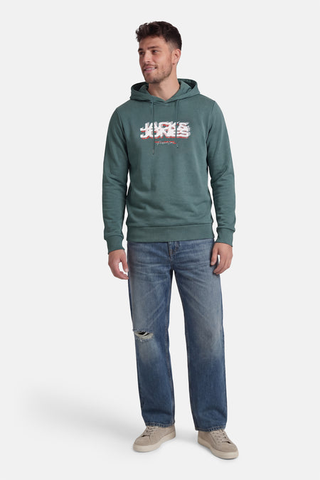 Groene sweater met kap van CORE BY JACK & JONES, met een logo op de borst, gecombineerd met jeans en sneakers.
