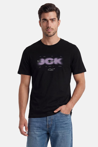 Zwart T-shirt van CORE BY JACK & JONES met paarse, wazige 'DCK & JONES' grafische print, gedragen door een man in jeans.