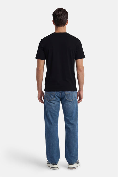 T-shirt noir à manches courtes de CORE BY JACK & JONES, uni, porté avec un jean bleu et des baskets.