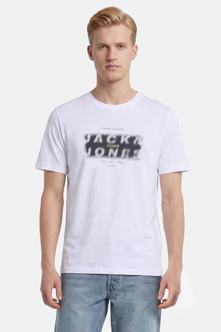 Wit T-shirt van CORE BY JACK & JONES met gesprayd zwart logo op de borst, gedragen door een man.