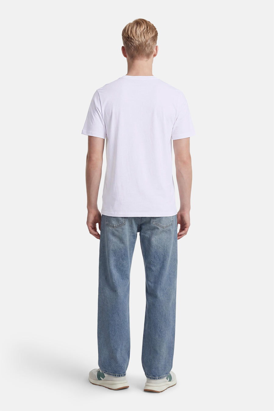 Wit T-shirt van CORE BY JACK & JONES, gedragen door een man, gezien van achteren, gecombineerd met een lichtblauwe spijkerbroek en sneakers.