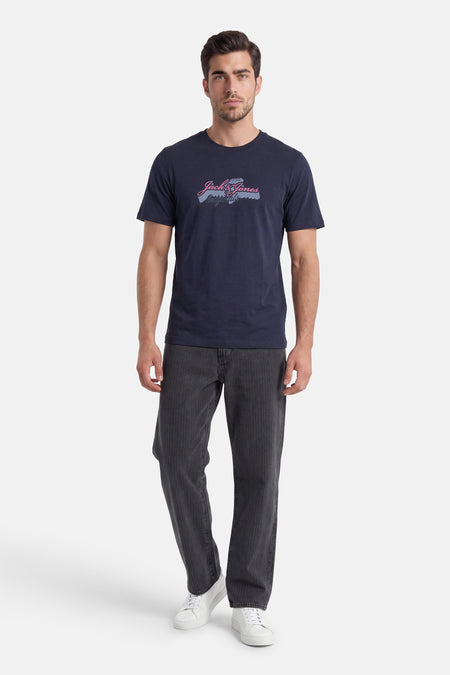 Donkerblauw T-shirt van ORIGINALS BY JACK & JONES met roze/blauwgrijze 'Jack & Jones Originals' print, gedragen met gestreepte jeans en witte sneakers.