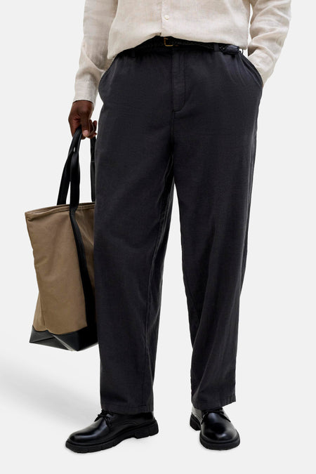 Pantalon de saison élastique noir pour homme de JACK & JONES JEANS INTELLIGENCE avec ceinture tissée, porté avec une chemise en lin et un sac.